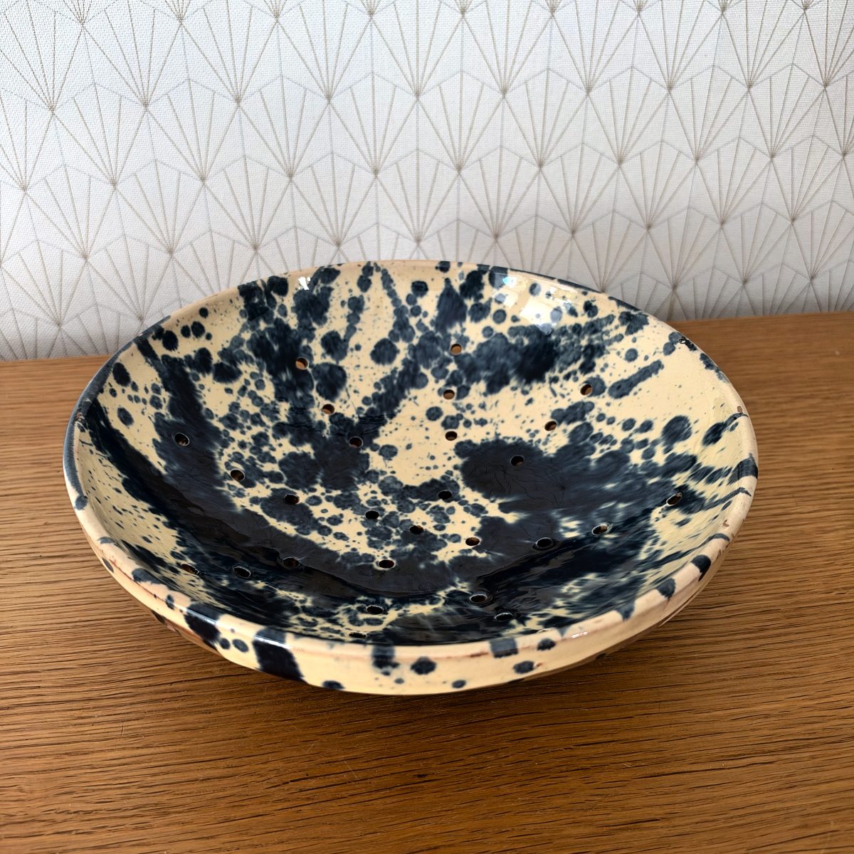 Top view of French ceramic berry colander bowl showing bold black splatter decoration and small drainage holes pierced across the interior.