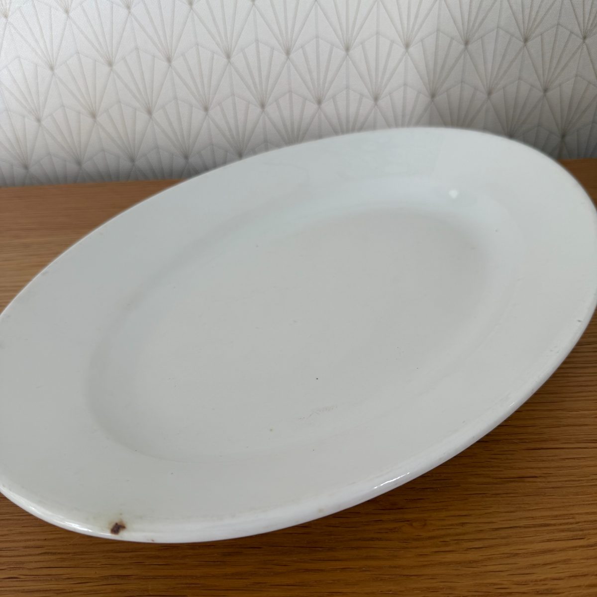 Overhead view of antique French white ironstone oval platter laid flat on oak table showing full oval form.
