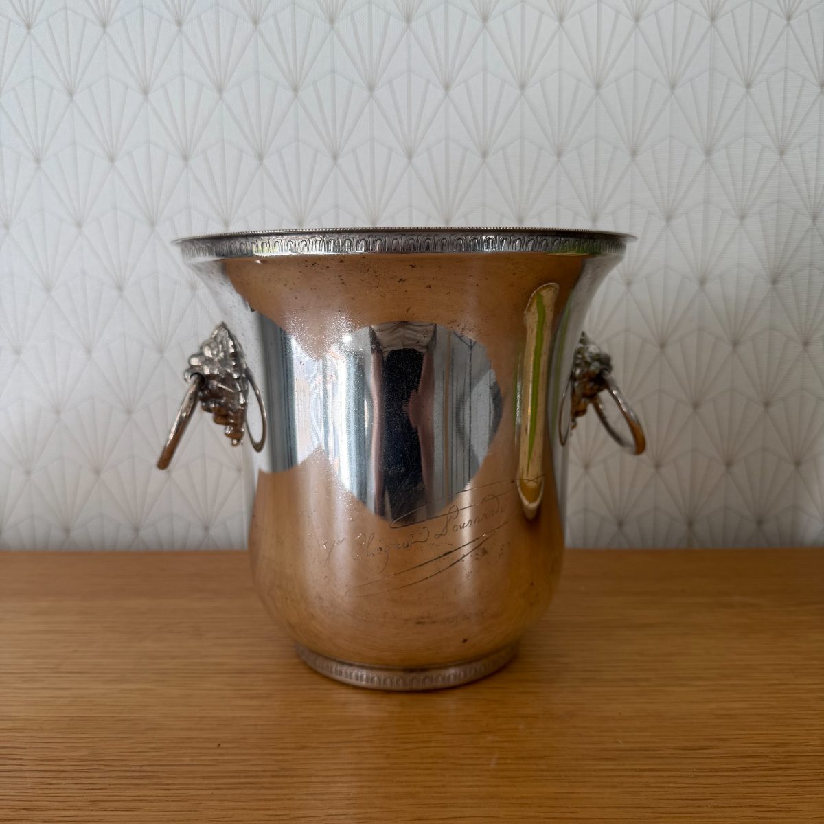 Side view of French silver plated champagne bucket with decorative lion head handles and flared rim, green label visible.