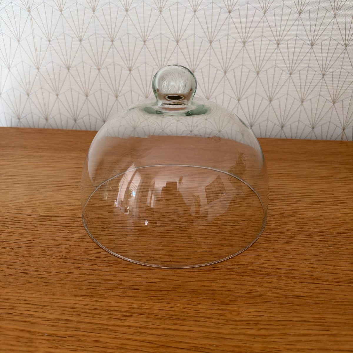 Vintage French clear glass cloche dome with ball knob at top, slightly closer view showing dome curvature and thin rim edge, reflections visible inside glass.