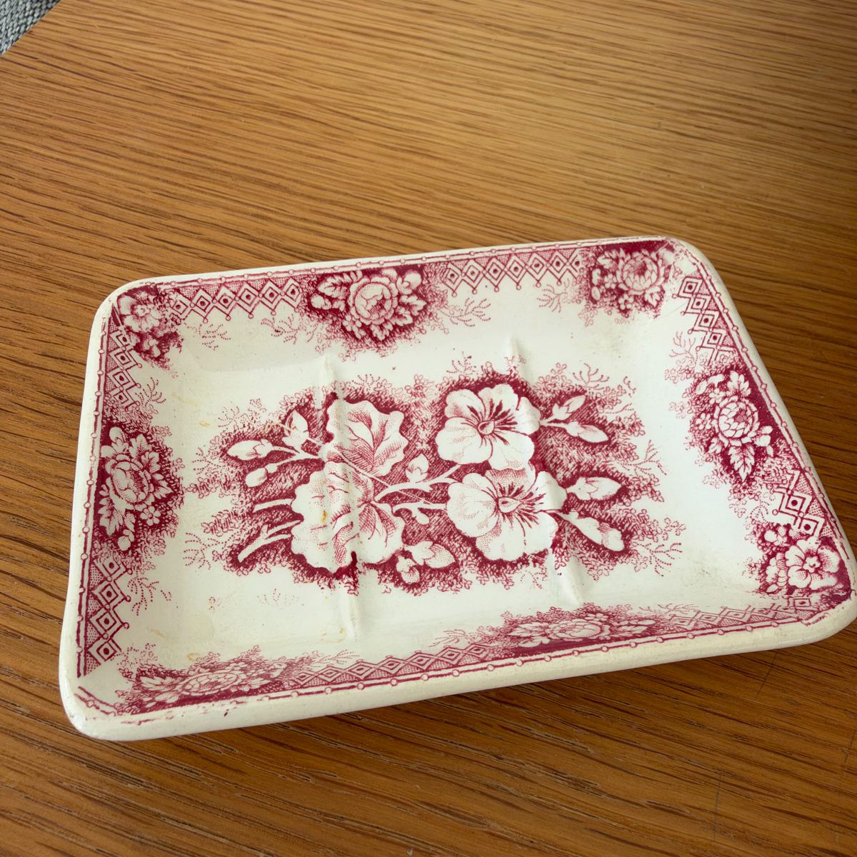Close-up of small rectangular red transferware soap dish with floral pansy motif and diamond border, crazing visible on white ironstone.
