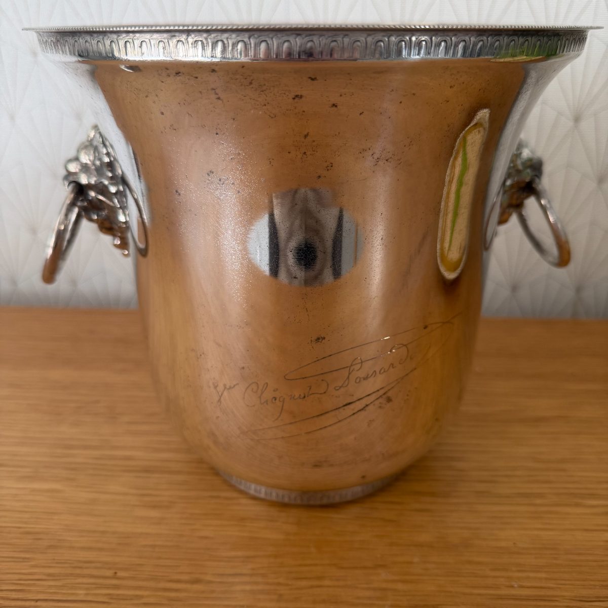 Close-up front view of engraved Veuve Clicquot script on silver plated champagne ice bucket with lion head handles.