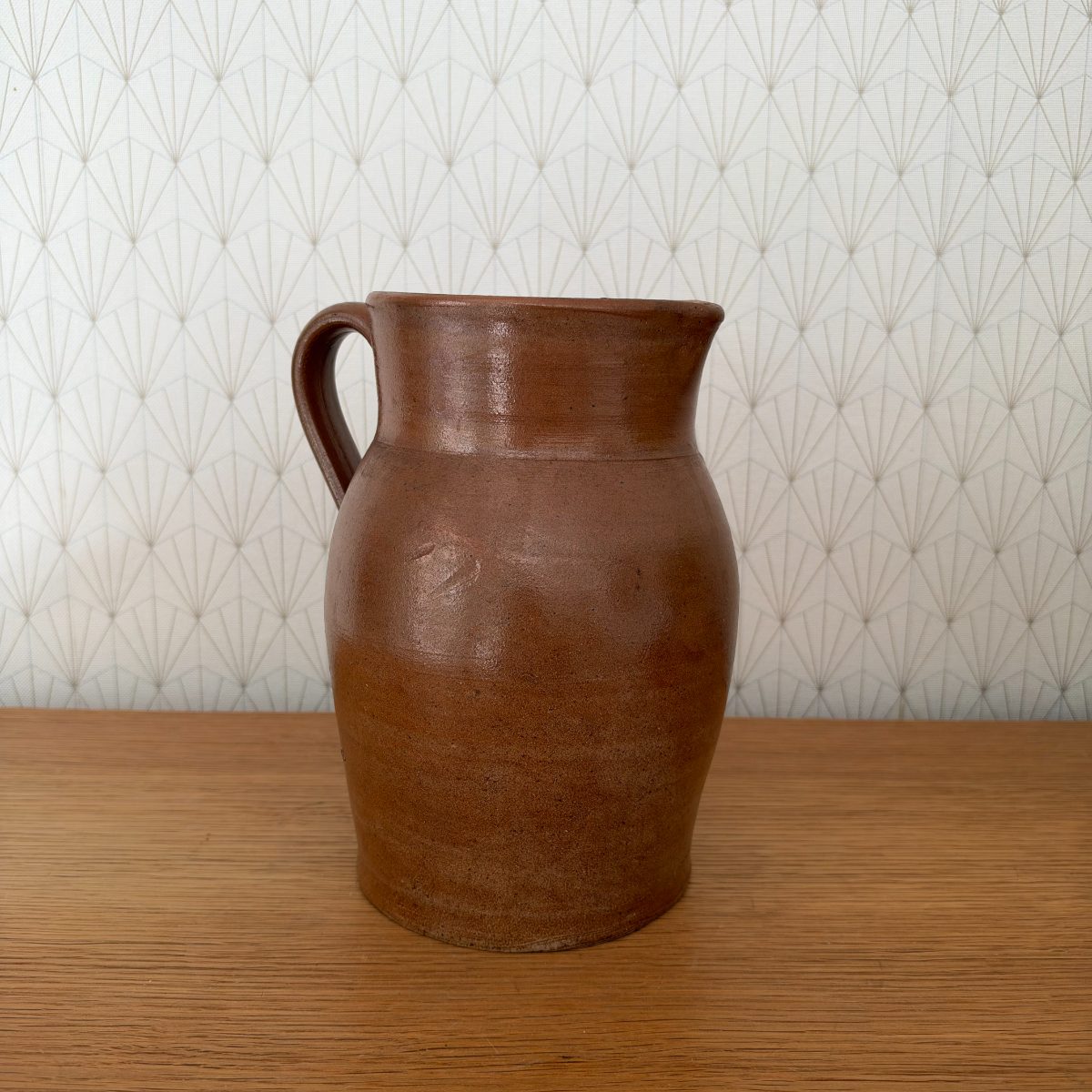 Antique French brown glazed stoneware pitcher showing bulbous body and pinched spout, side view.