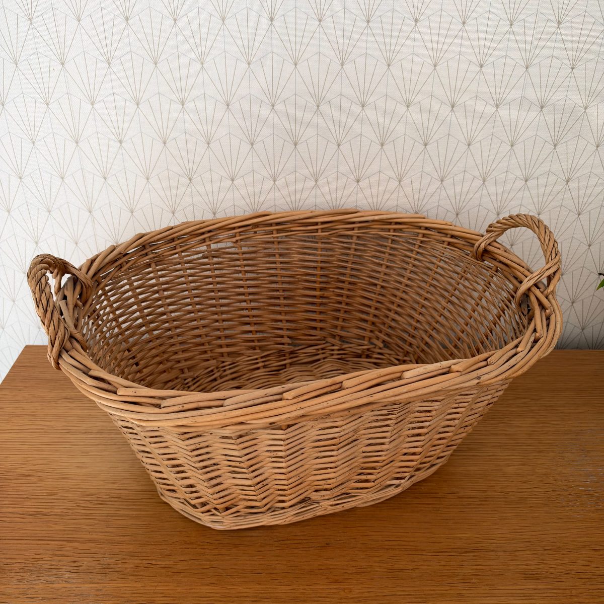 Overhead three-quarter view of vintage French wicker laundry basket showing open top and woven rattan interior with two side handles.