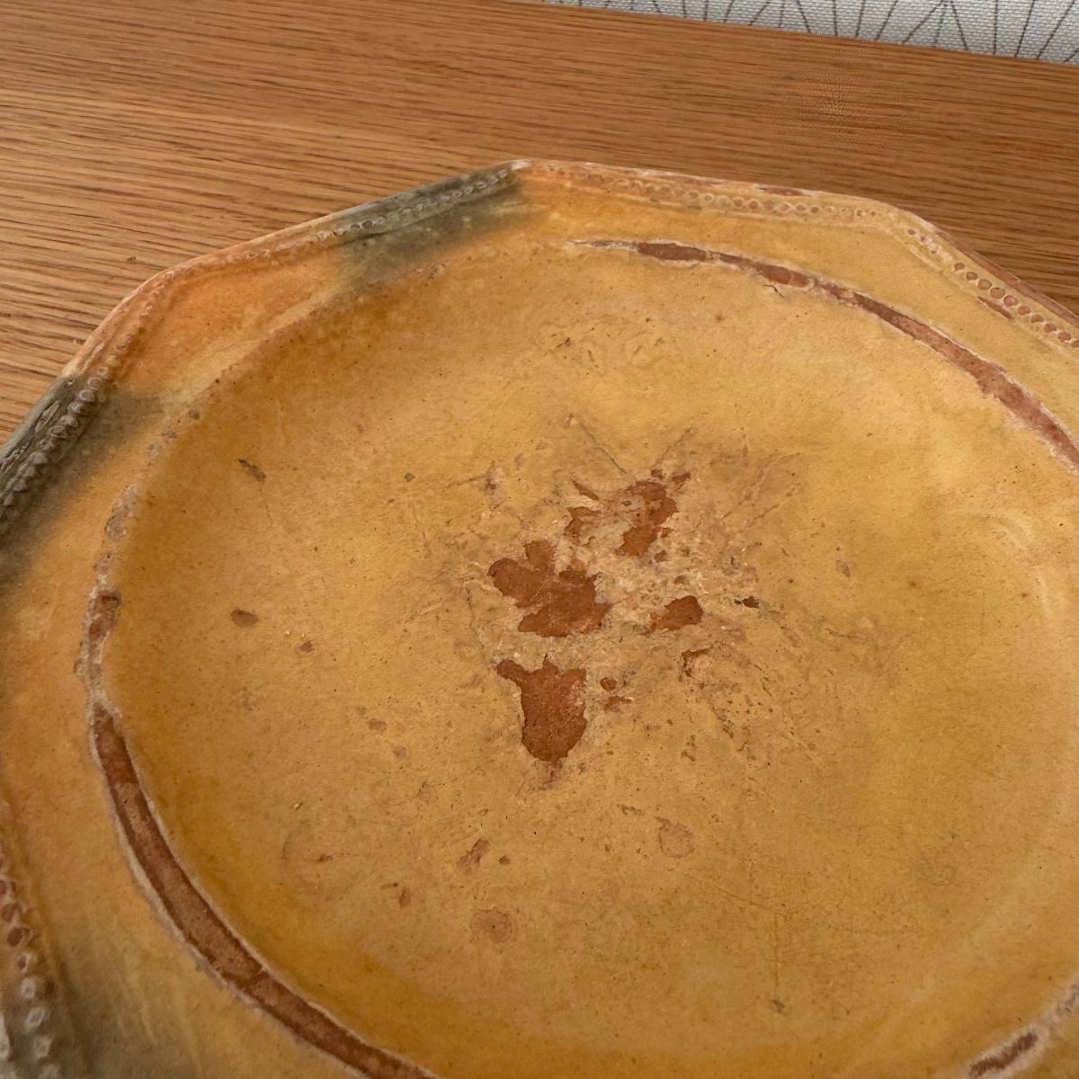 Close-up of antique French terracotta plate interior showing amber glaze with russet wear spots and incised ring.