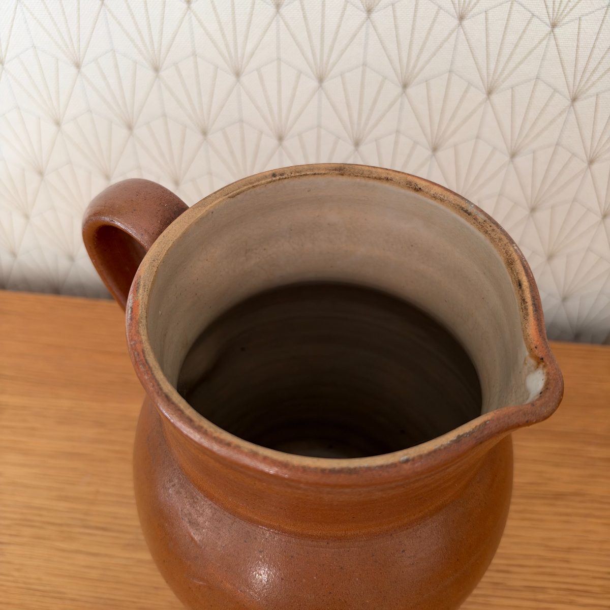 Top-down view into antique French stoneware pitcher showing unglazed interior rim and dark well.