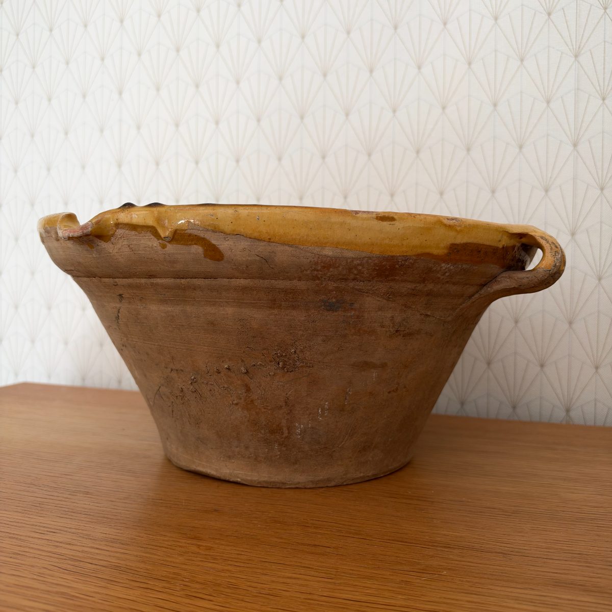 Side view of antique French terracotta tian bowl showing unglazed earthenware exterior with tool marks, surface cracks, and one visible loop handle.