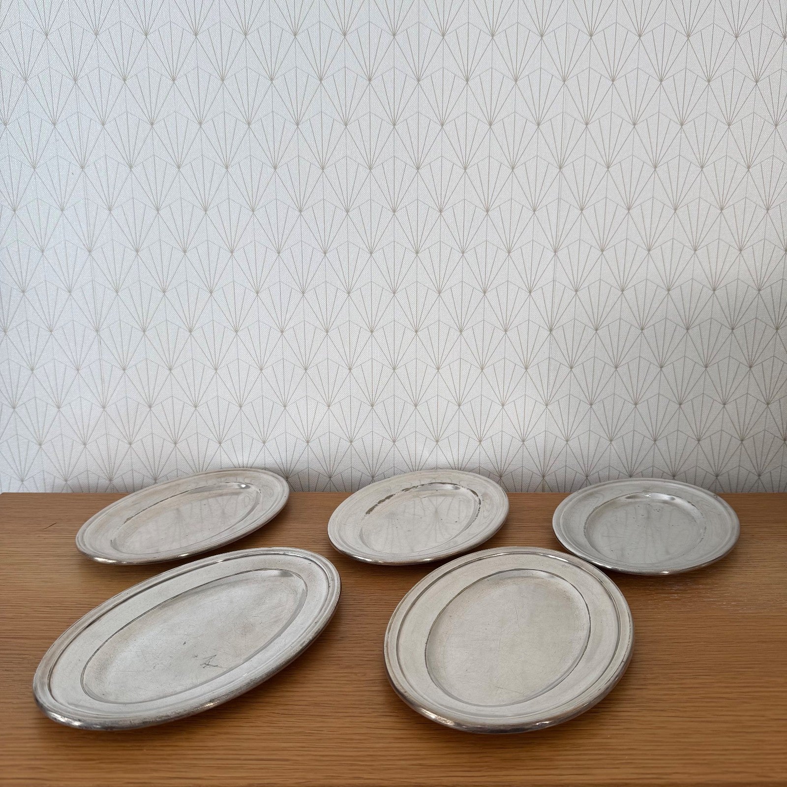 Five French silver plated oval serving trays arranged on wooden table with geometric wallpaper background
