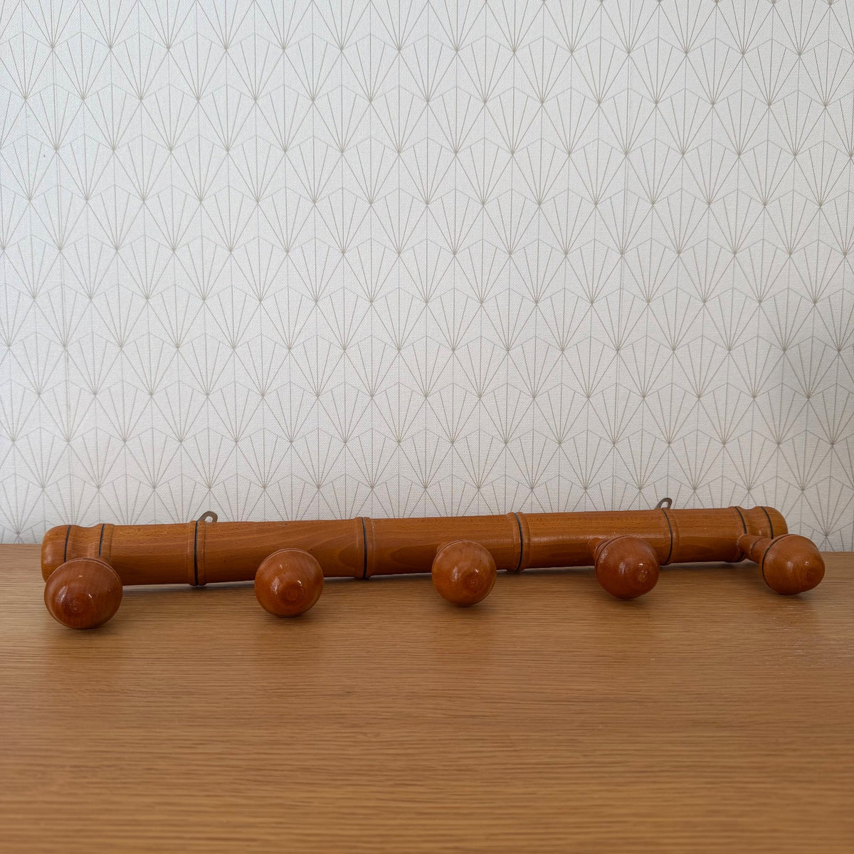 Vintage French bamboo coat rack with five acorn pegs, side view against patterned wallpaper