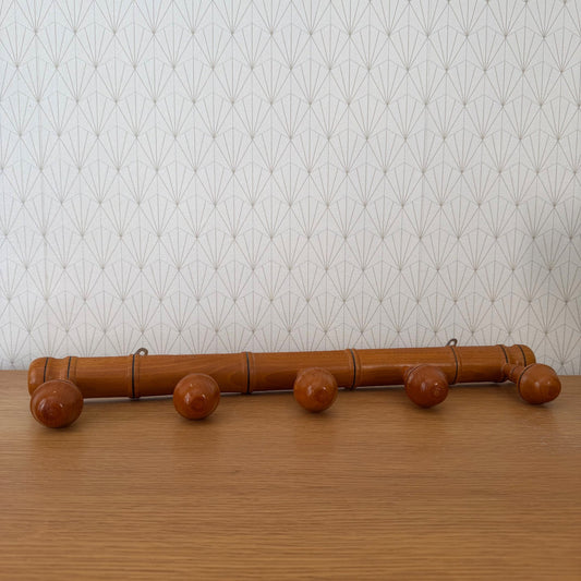 Vintage French bamboo coat rack with five acorn pegs, side view against patterned wallpaper