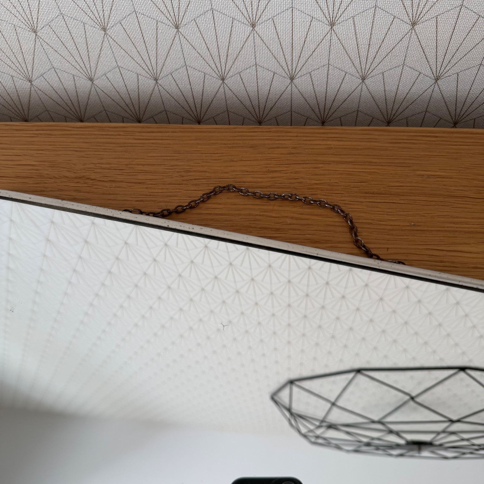 Close-up detail of chrome metal frame and copper-toned chain attachment on French Art Deco mirror