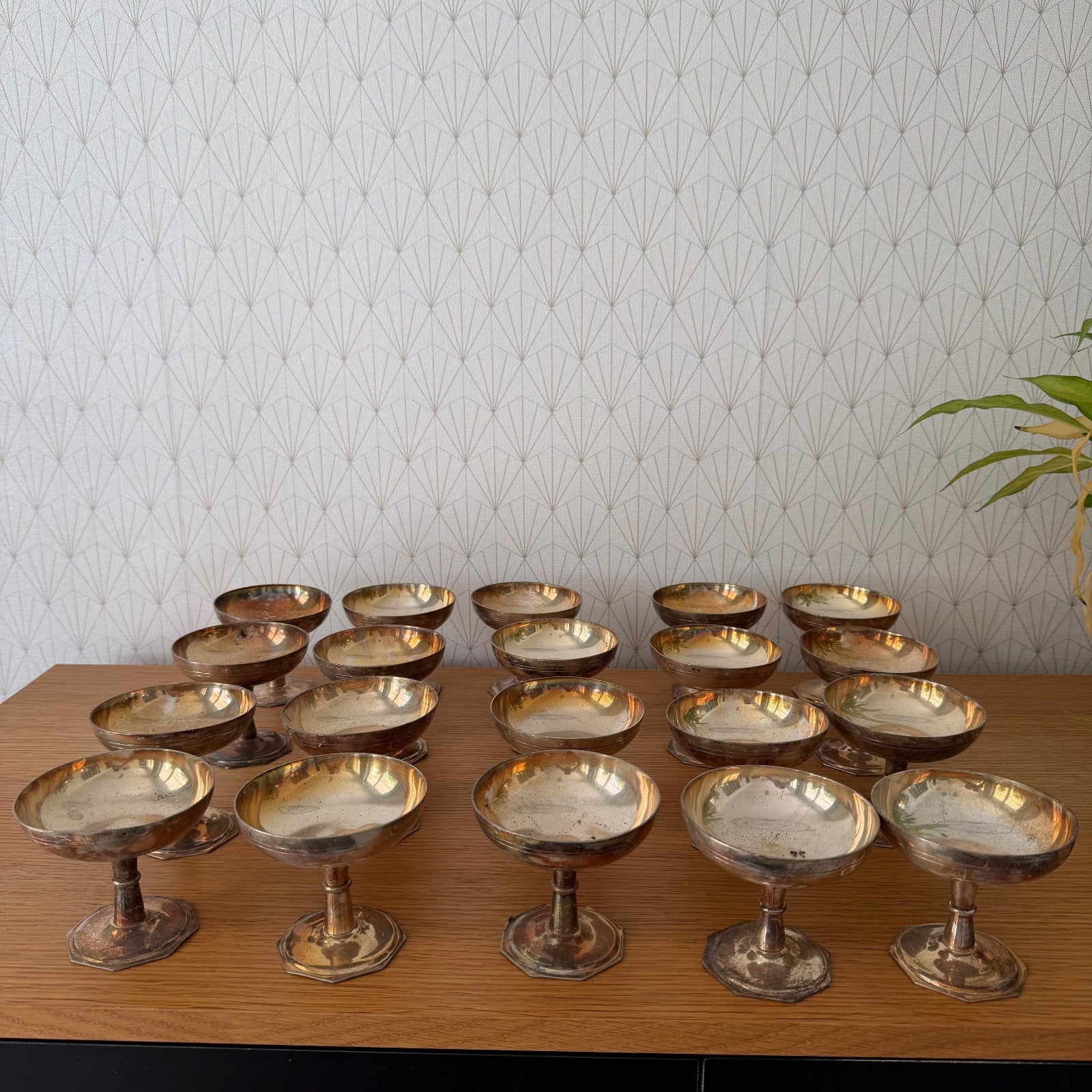 Set of 20 vintage French silverplate champagne coupes arranged on wooden table with fan-patterned wallpaper background