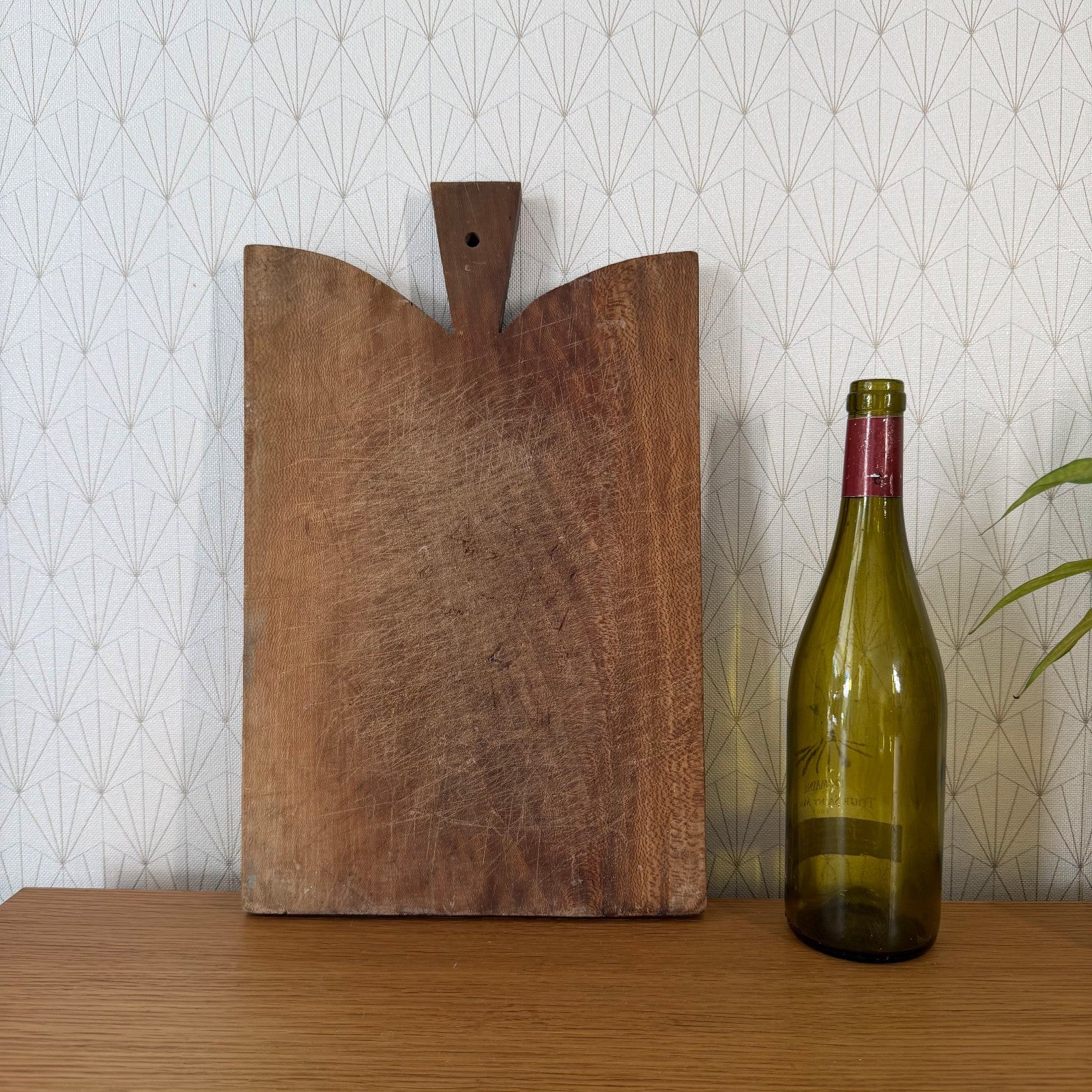 French antique bread board with double-lobed edge and central handle, displayed with wine bottle for scale