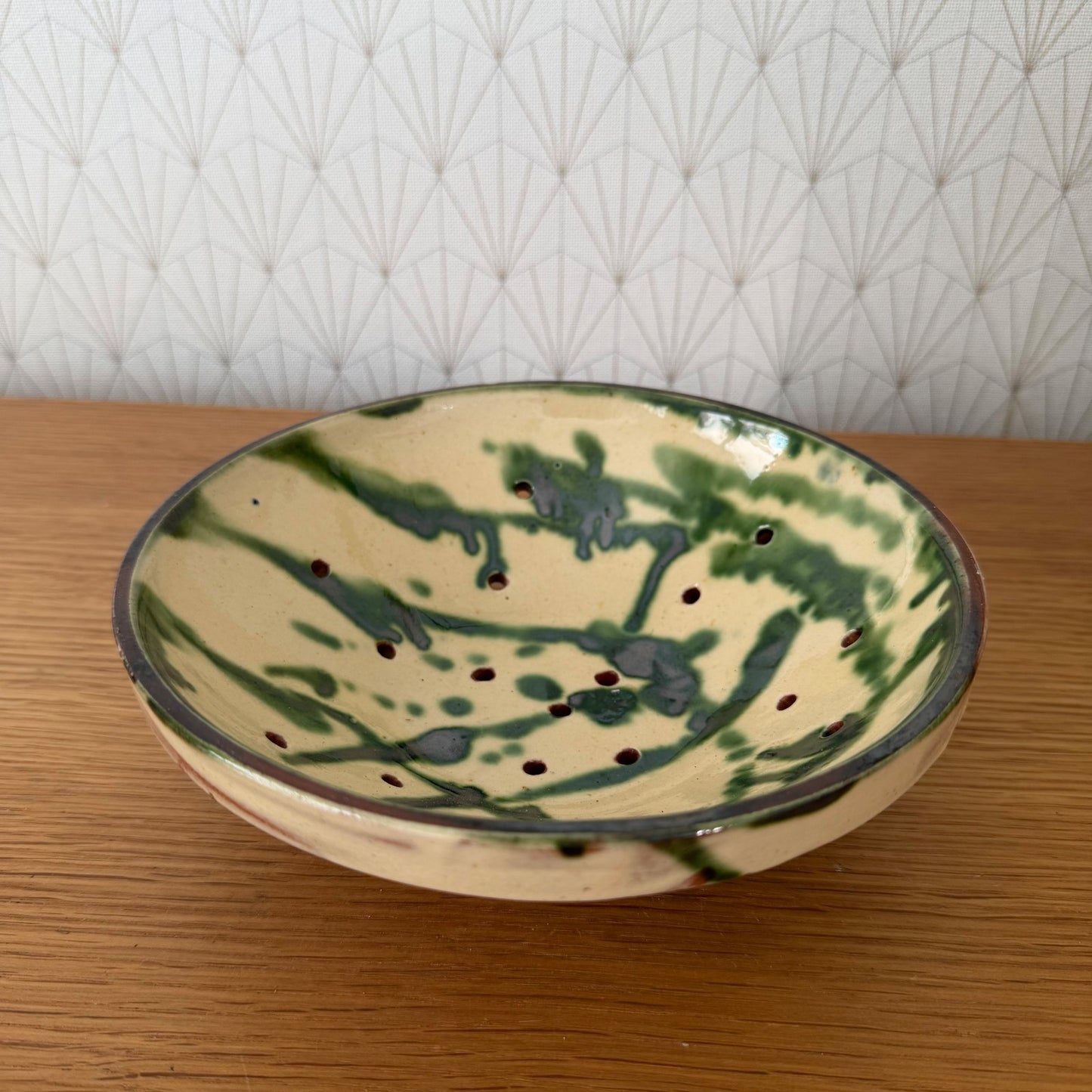 French pottery fruit bowl with green painted leaf design and brown drainage holes, flat lay