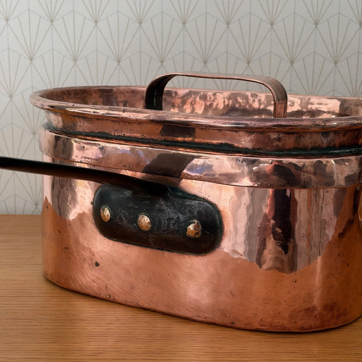 Antique French copper braising pan displayed from angle showing depth, handle, and oval shape