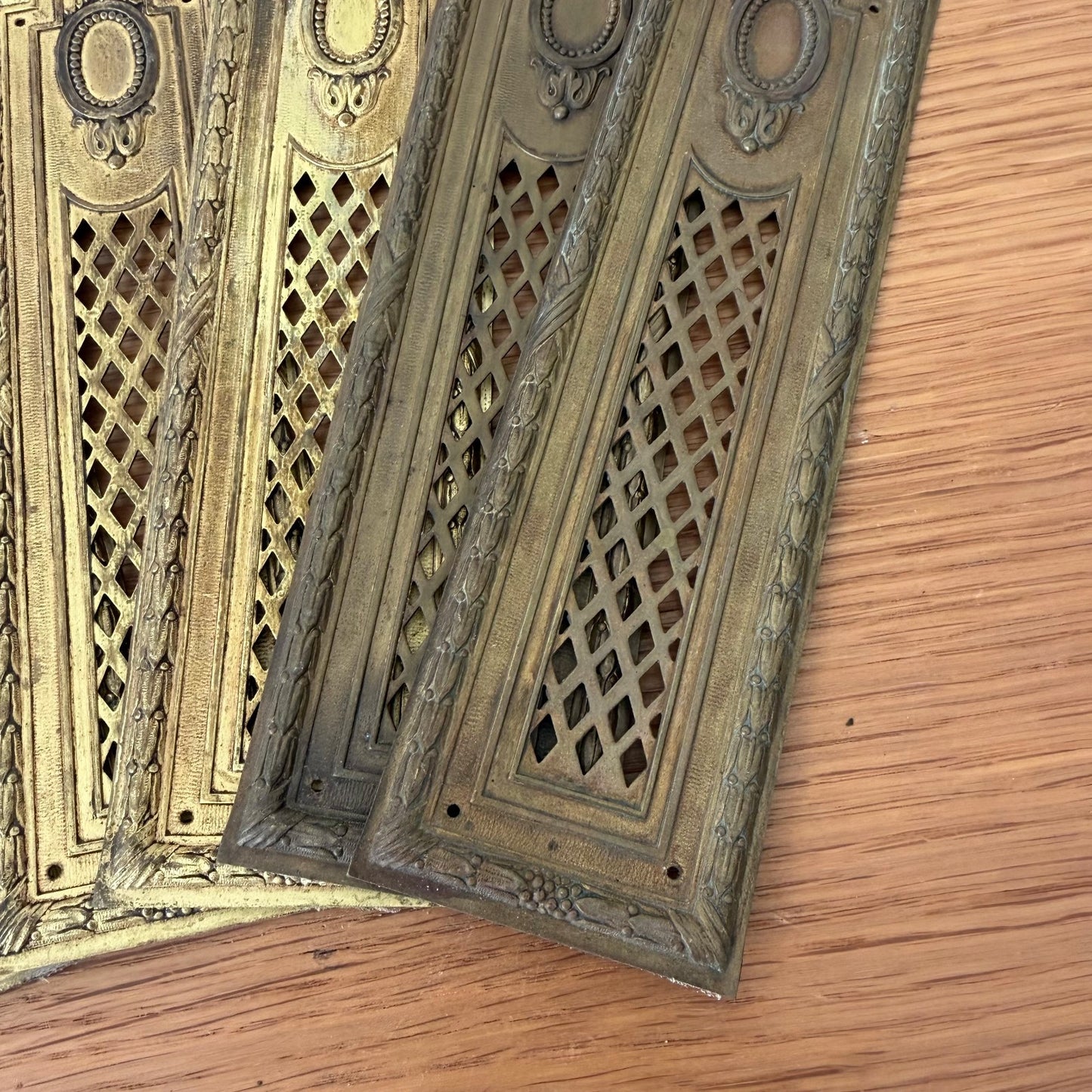 Angled view of French vintage brass door plates displaying raised ornamental design and diamond cutout details