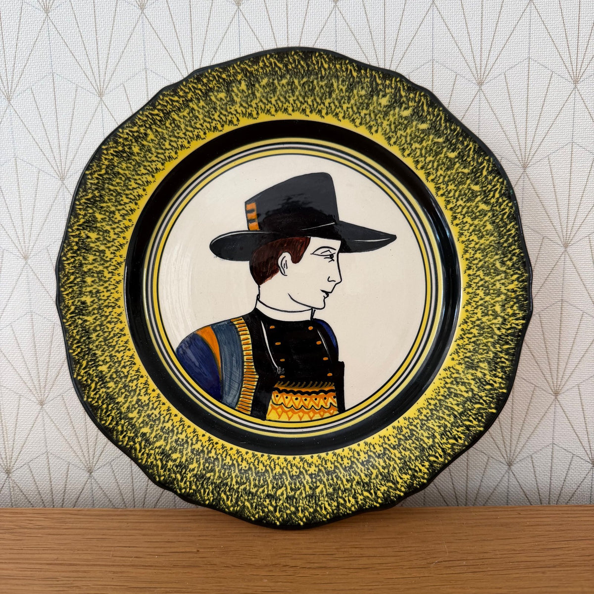 Henriot Quimper man's portrait plate with yellow speckled border, black hat, and blue and gold costume details