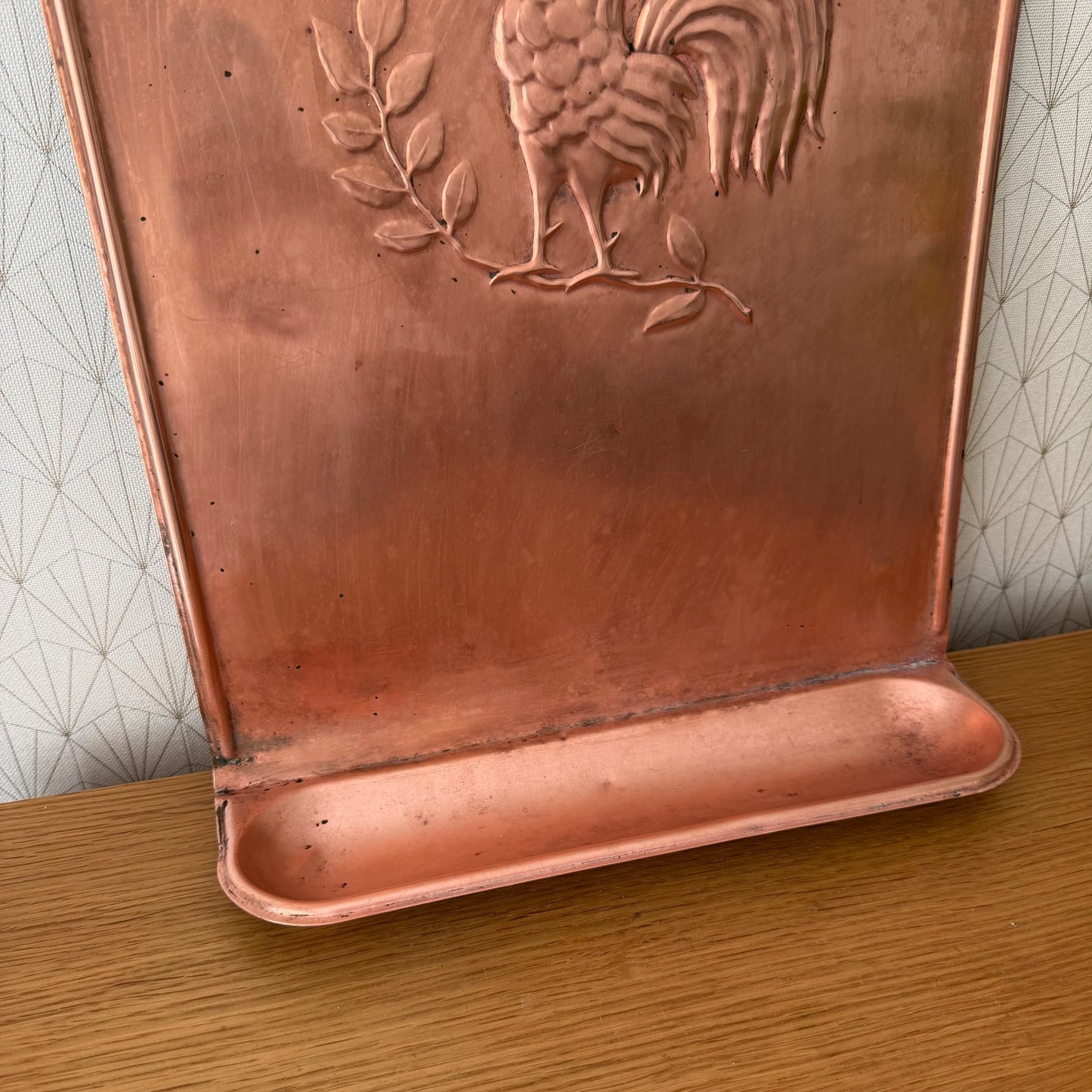 Detailed view of rooster and botanical relief on copper utensils hanger