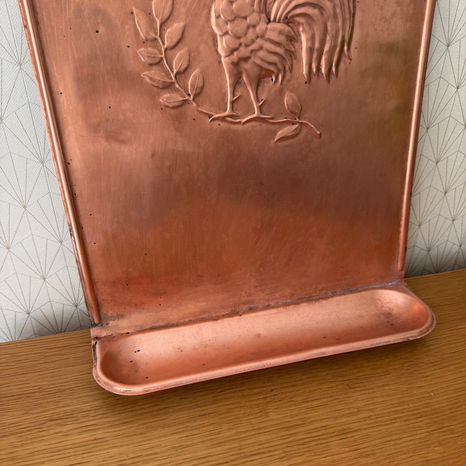 Detailed view of rooster and botanical relief on copper utensils hanger