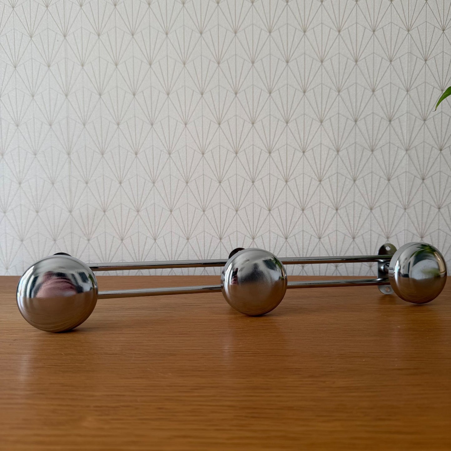 Three chrome spherical coat hooks mounted on dual horizontal rods, front view against geometric wallpaper