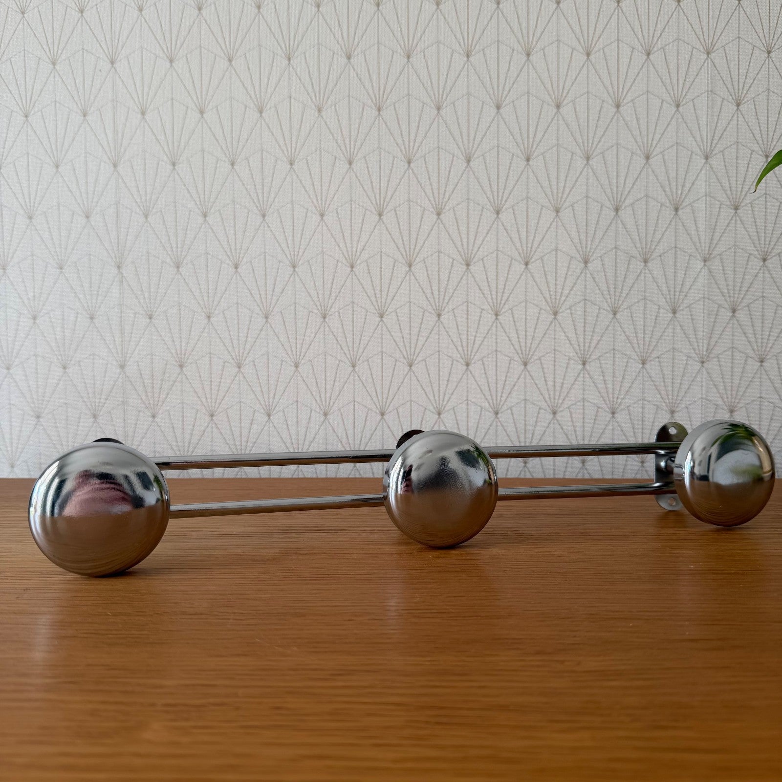 Three chrome spherical coat hooks mounted on dual horizontal rods, front view against geometric wallpaper
