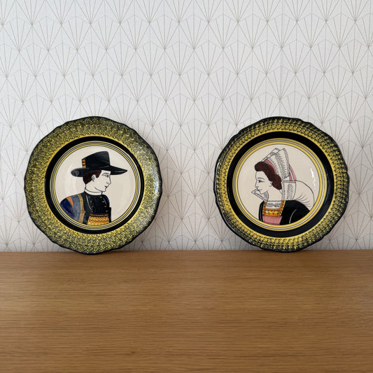 Pair of Henriot Quimper portrait plates with hand-painted Breton man in black hat and woman in traditional dress against patterned background