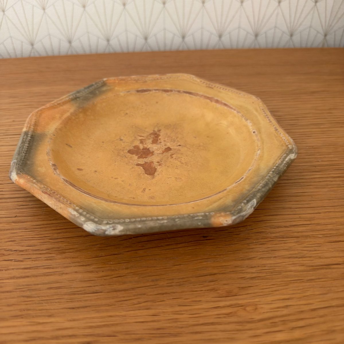 Top angled view of antique French octagonal terracotta plate showing amber glaze and dotted rim detail.