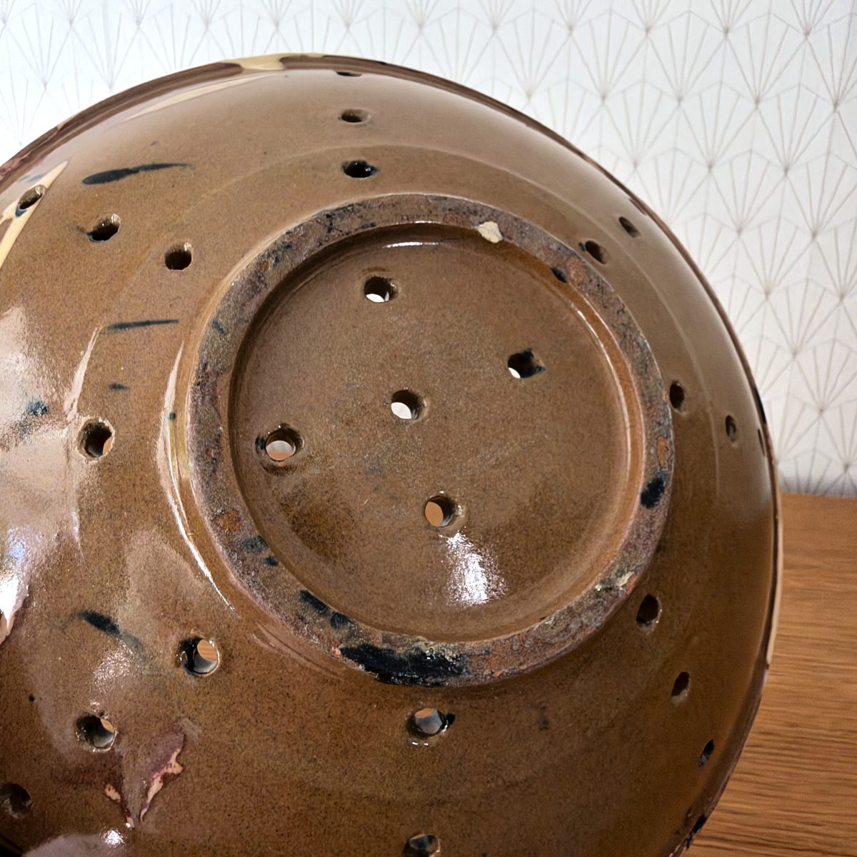 Underside of French earthenware colander bowl showing brown glazed base with multiple hand-pierced drainage holes and foot ring detail.