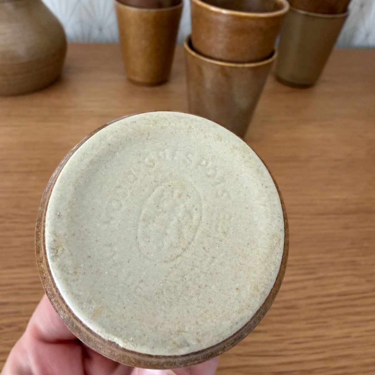 Impressed maker mark on the unglazed base of a French vintage stoneware cup with other cups and pitcher in background