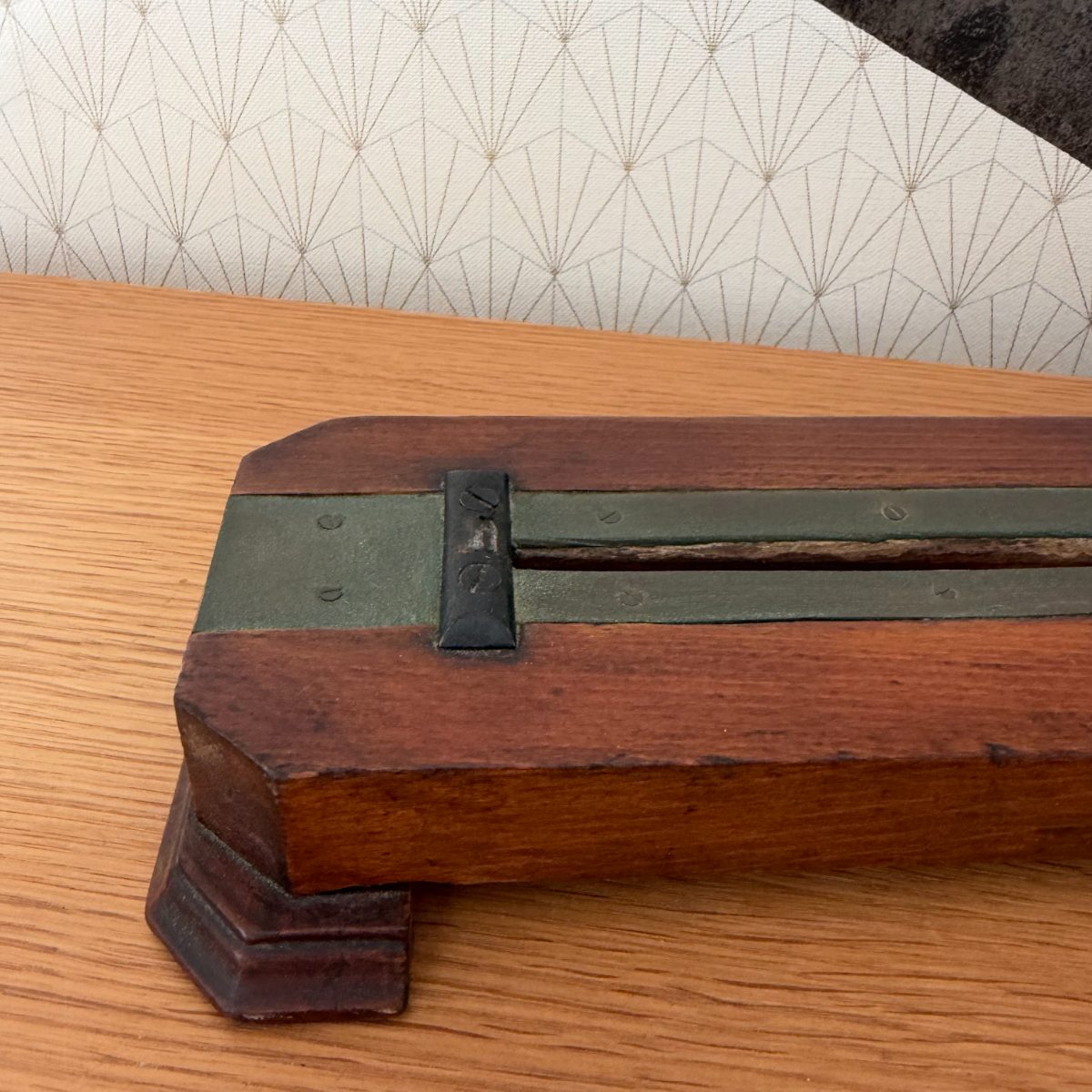Underside close-up of antique French bread slicer wooden base showing green-painted metal channel guides riveted along the length.