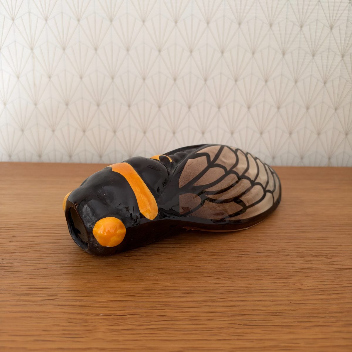 Vintage French hand-painted ceramic cicada figurine in black and amber orange, side view showing wing detail and open mouth, on wood surface.