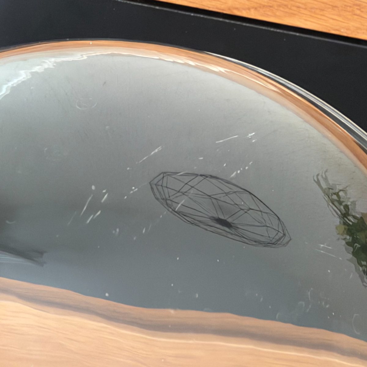 Interior view of vintage French glass cloche dome lying on side, showing condensation marks, light scratches on inner surface, and small wire decorative object reflected inside.