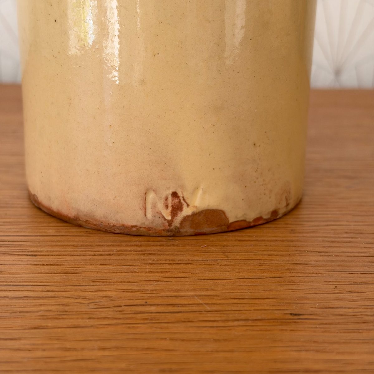 Close-up of base of antique French stoneware crock showing glaze loss and wear along the lower edge and foot.