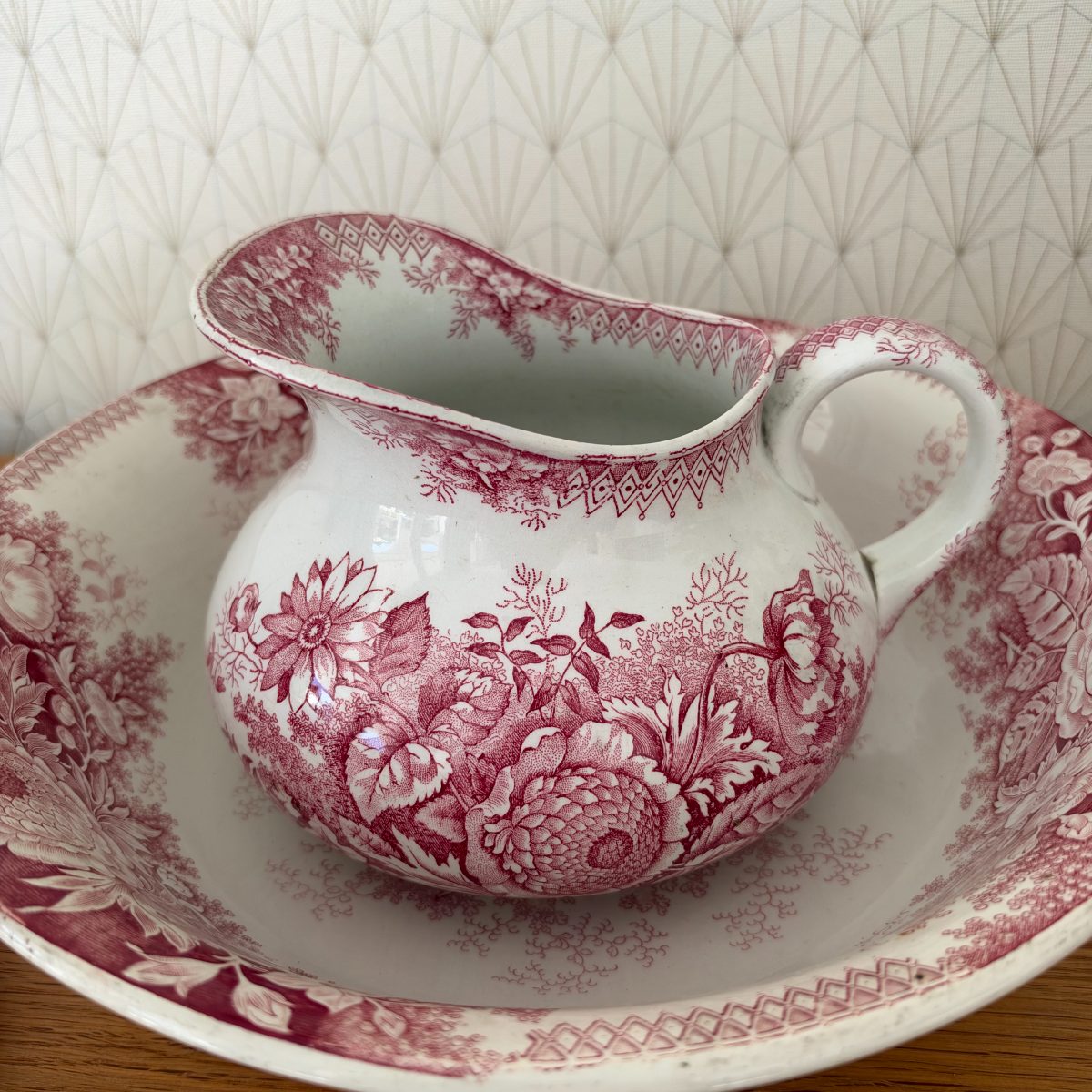 Close-up of red transferware ironstone pitcher showing detailed floral transfer pattern, spout interior with diamond border, and loop handle.