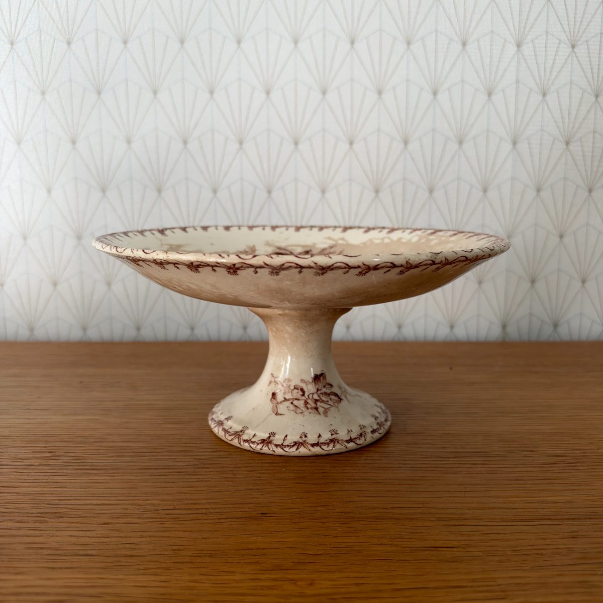 Antique French Gien transferware pedestal cake stand, cream ironstone with brown floral and vine decoration, side view on wooden table.