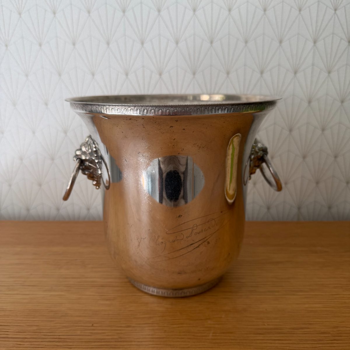 Vintage French silver plated champagne ice bucket with lion head ring handles and engraved Veuve Clicquot script, front view on oak surface.