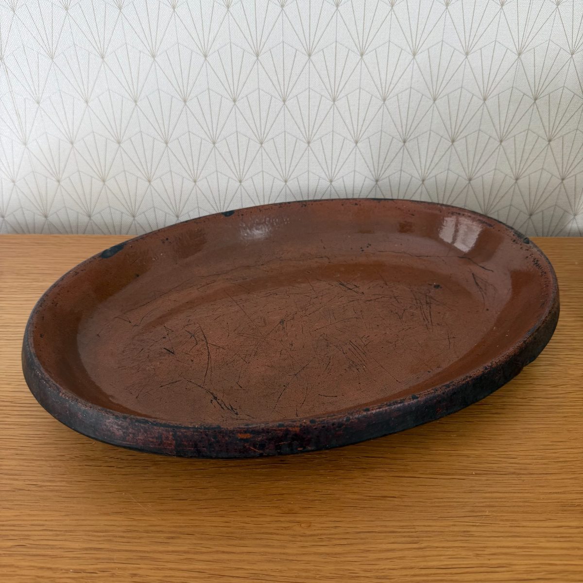 Front three-quarter view of the oval French earthenware baking dish showing dark unglazed exterior rim and warm brown interior glaze.