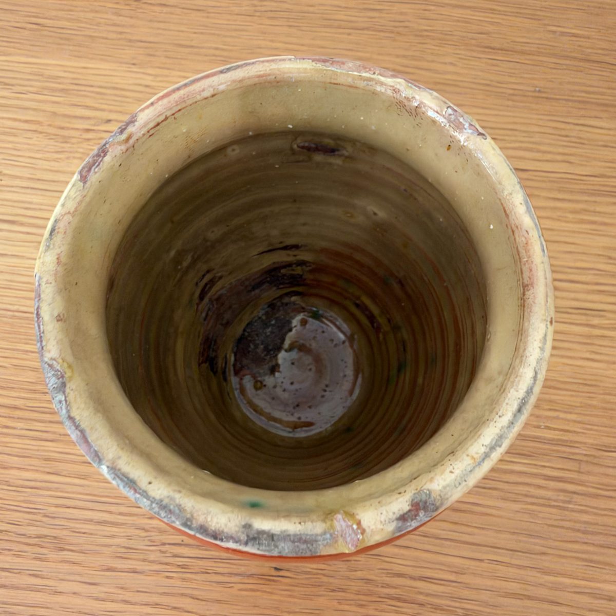 Overhead view inside antique French earthenware pot showing cream interior glaze with dark brown center and concentric throwing marks.