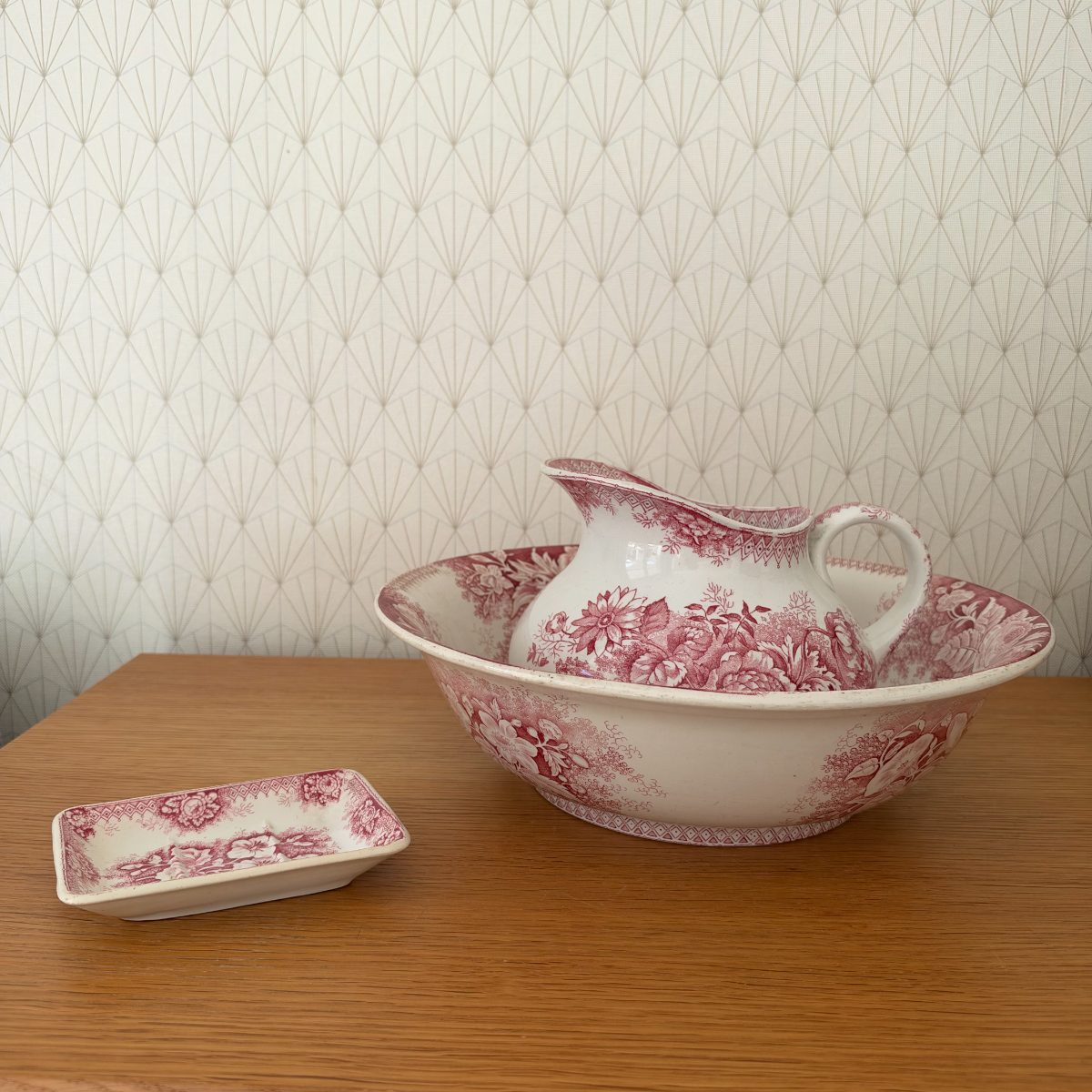 Antique red transferware wash set with large ironstone basin, matching pitcher and small rectangular soap dish displayed on oak table, floral pink pattern.
