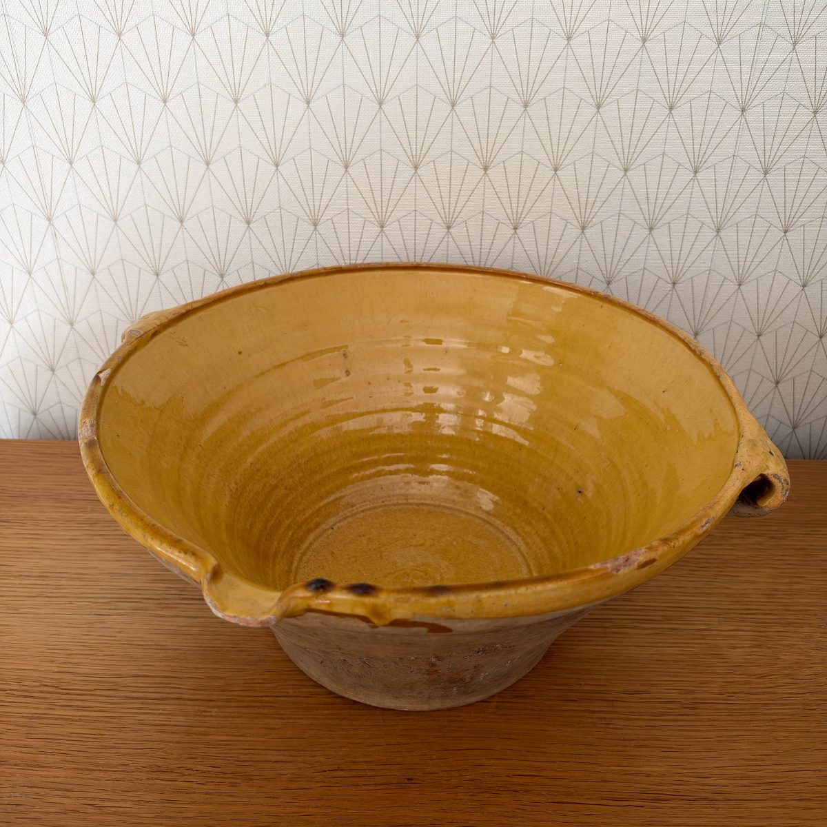 Front-angle view of antique French terracotta tian bowl showing ochre glazed interior with concentric wheel rings and small pinched spout detail at rim.