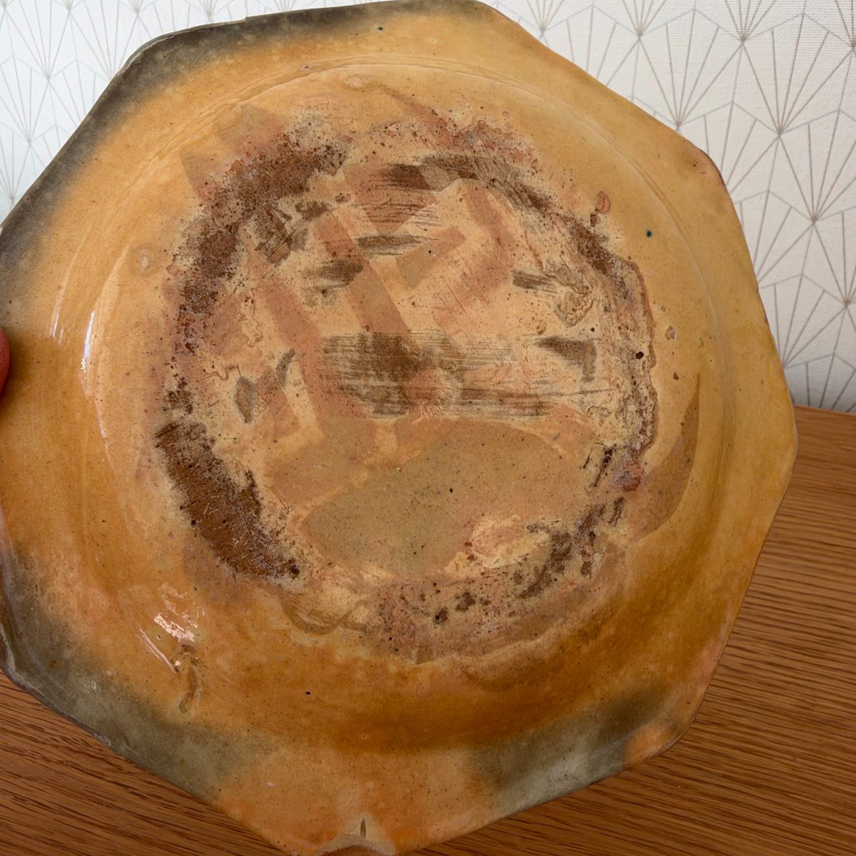 Underside of antique French octagonal earthenware plate showing kiln marks, unglazed foot and amber glaze base.