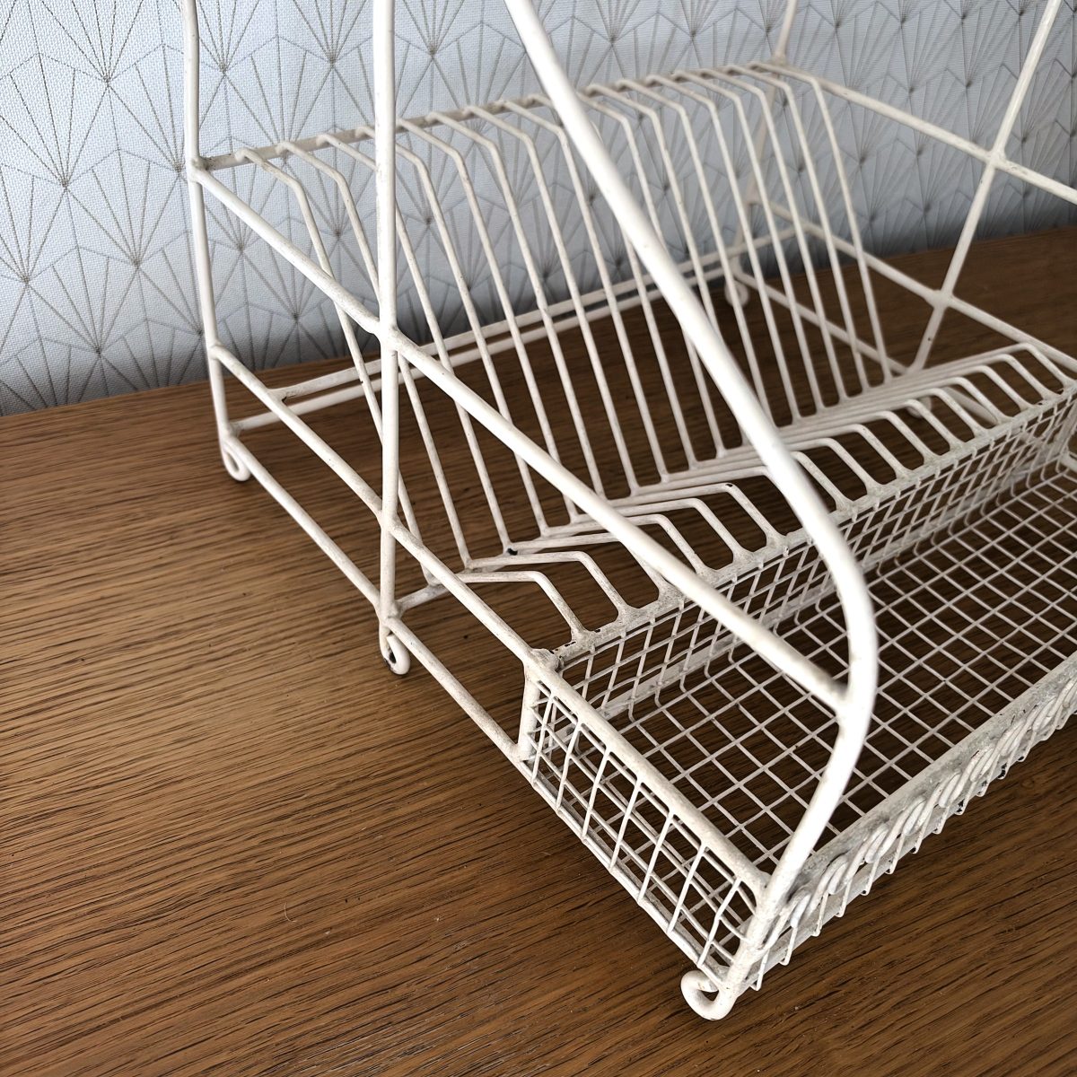 Side angle close-up of the lower section of a vintage French wire egouttoir showing plate dividers and wire mesh drip tray on a wood surface.