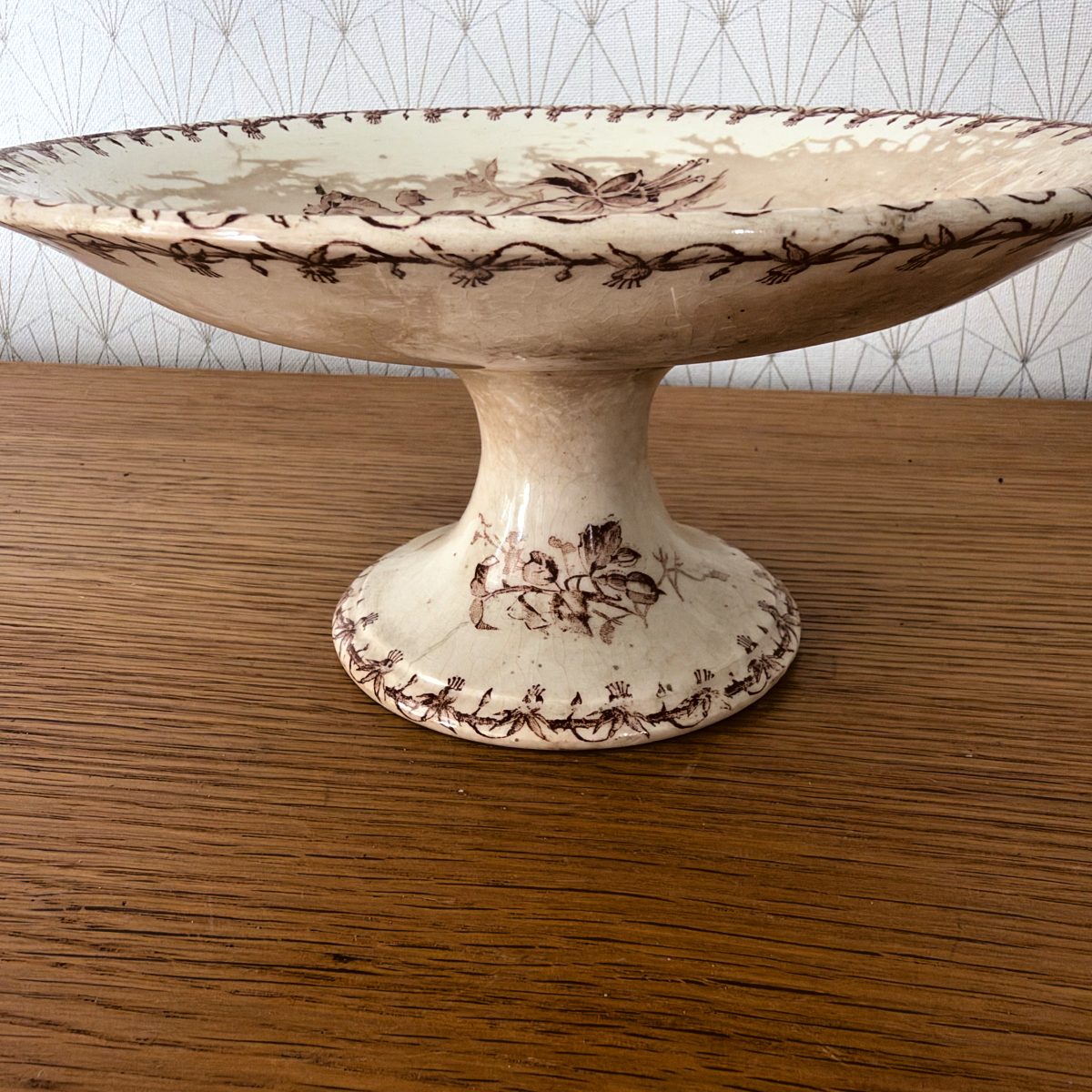 Close-up side view of the Gien pedestal cake stand showing crazing, floral motif on the base foot and vine border detail.