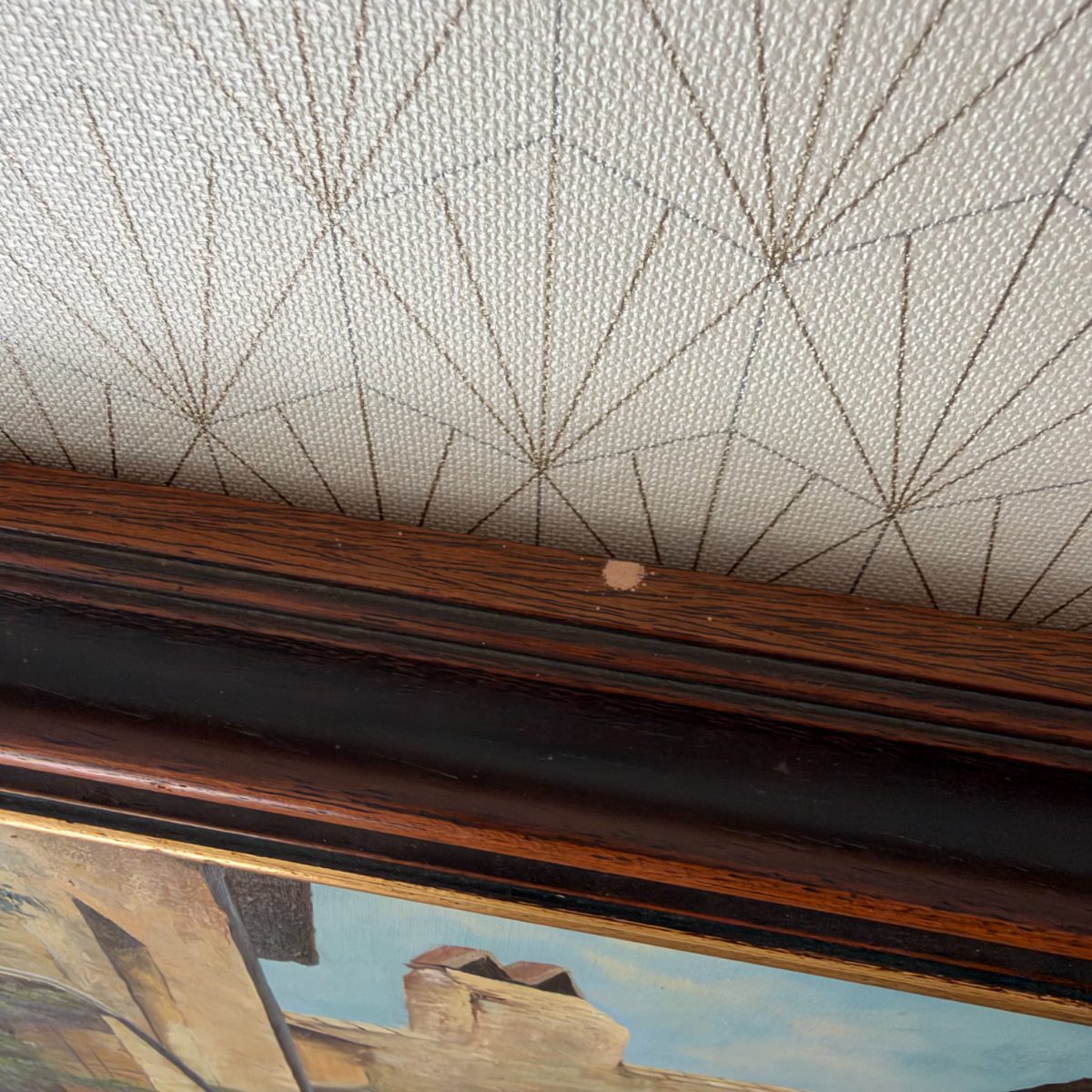 Detail of the dark wood and black frame top edge of the Dorgendial French village oil painting, showing minor wear consistent with age.