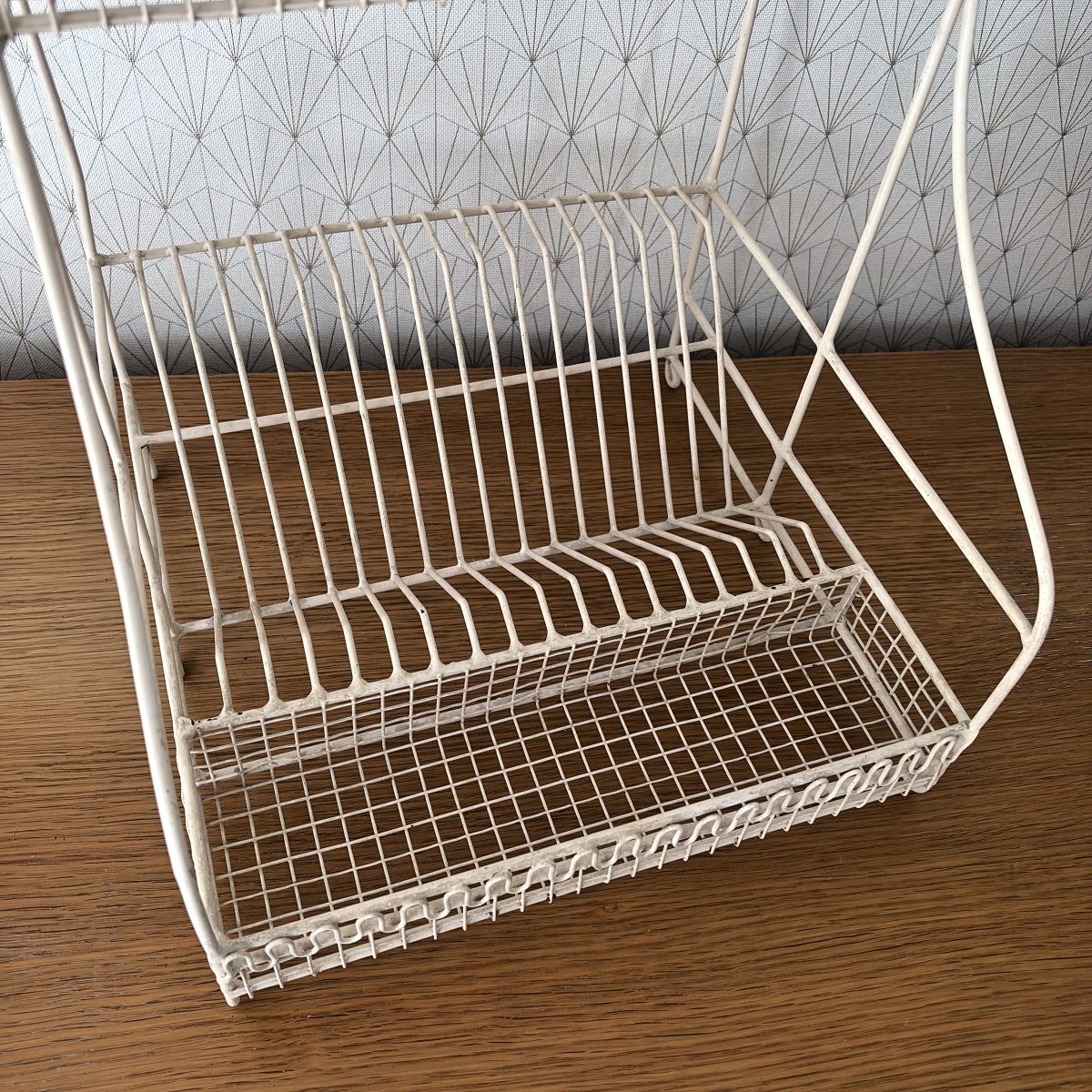 Angled view of the lower tier of a French white wire dish rack showing vertical plate slots and shallow wire drip tray basket below.