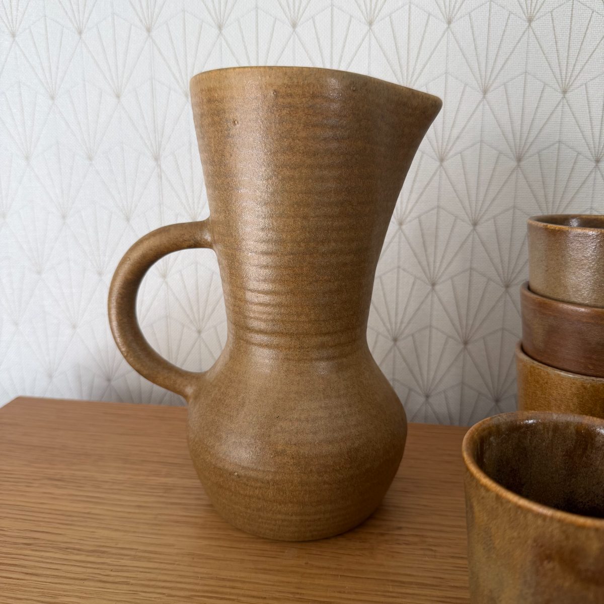 Close-up of French studio pottery pitcher showing ribbed texture, flared spout, loop handle and matte ochre glaze