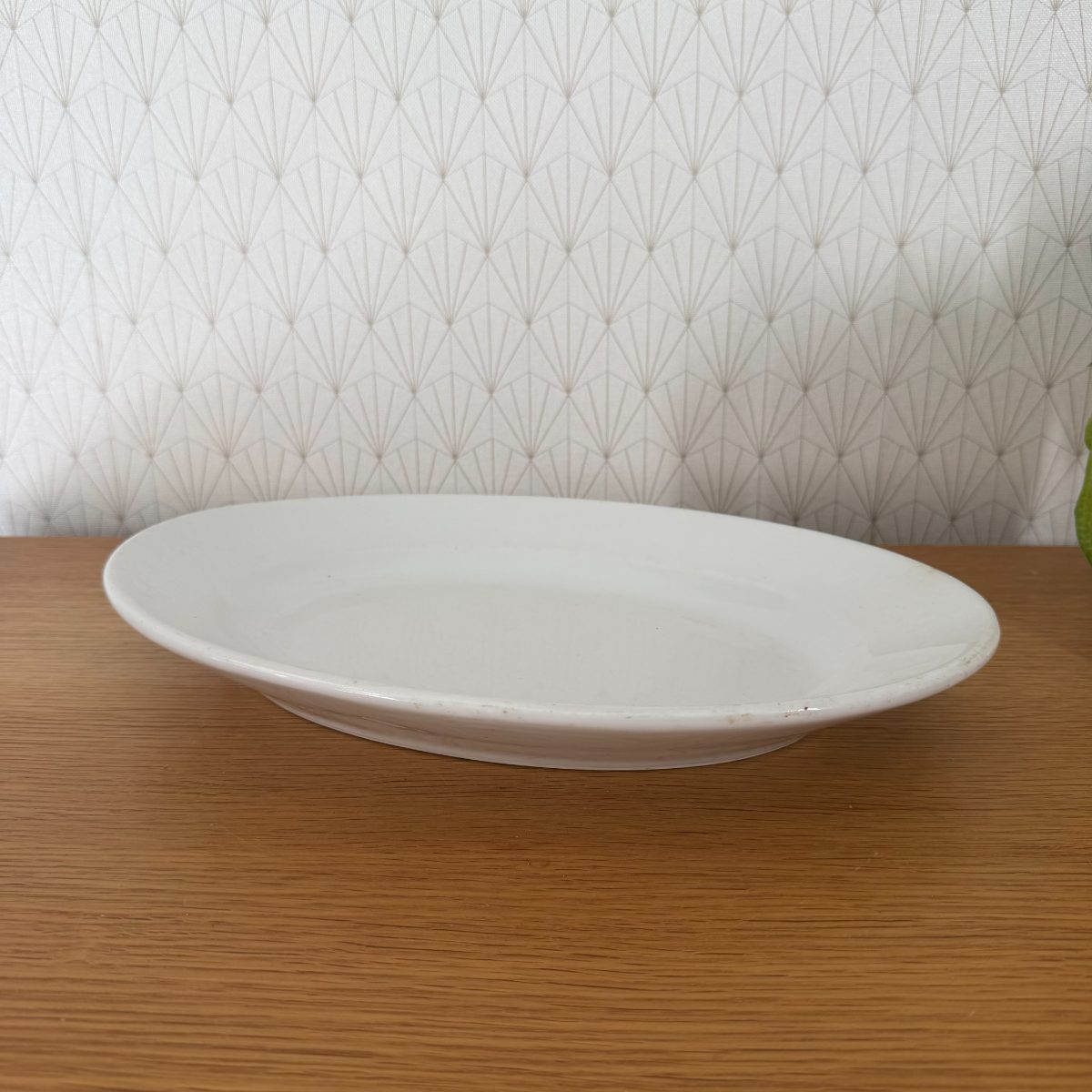 Antique French white ironstone oval serving platter shown from side angle on oak surface, creamy glaze with gentle patina.