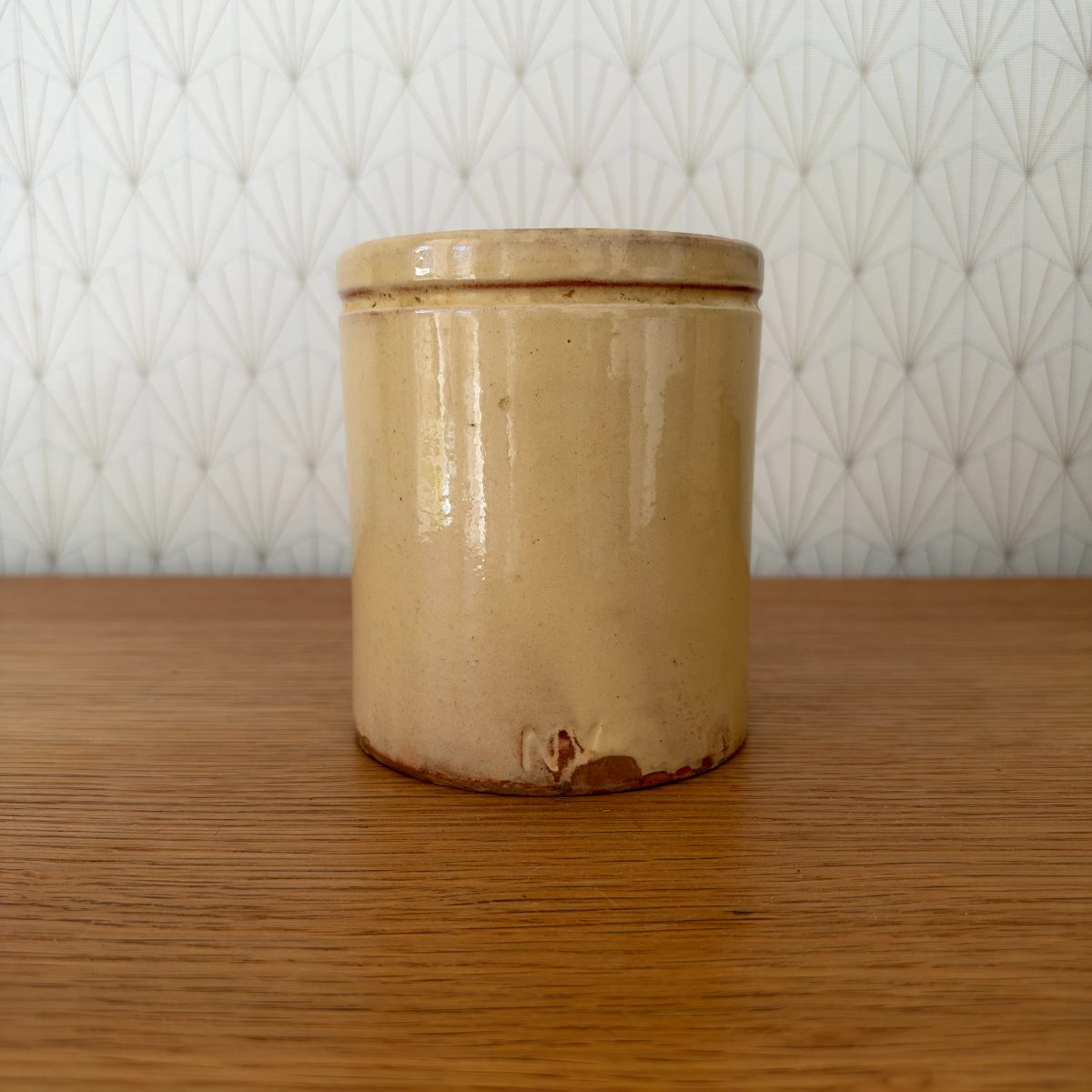 Side view of antique French pot a confiture showing smooth ochre yellow glazed body with glaze drips and worn base.