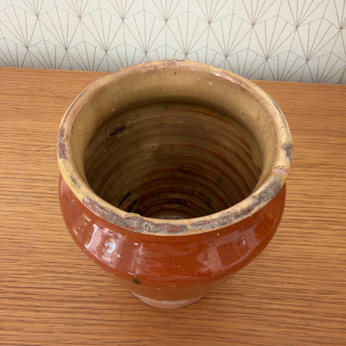Top-down view into antique French earthenware pot showing cream and olive-brown interior glaze with visible wheel throwing rings.