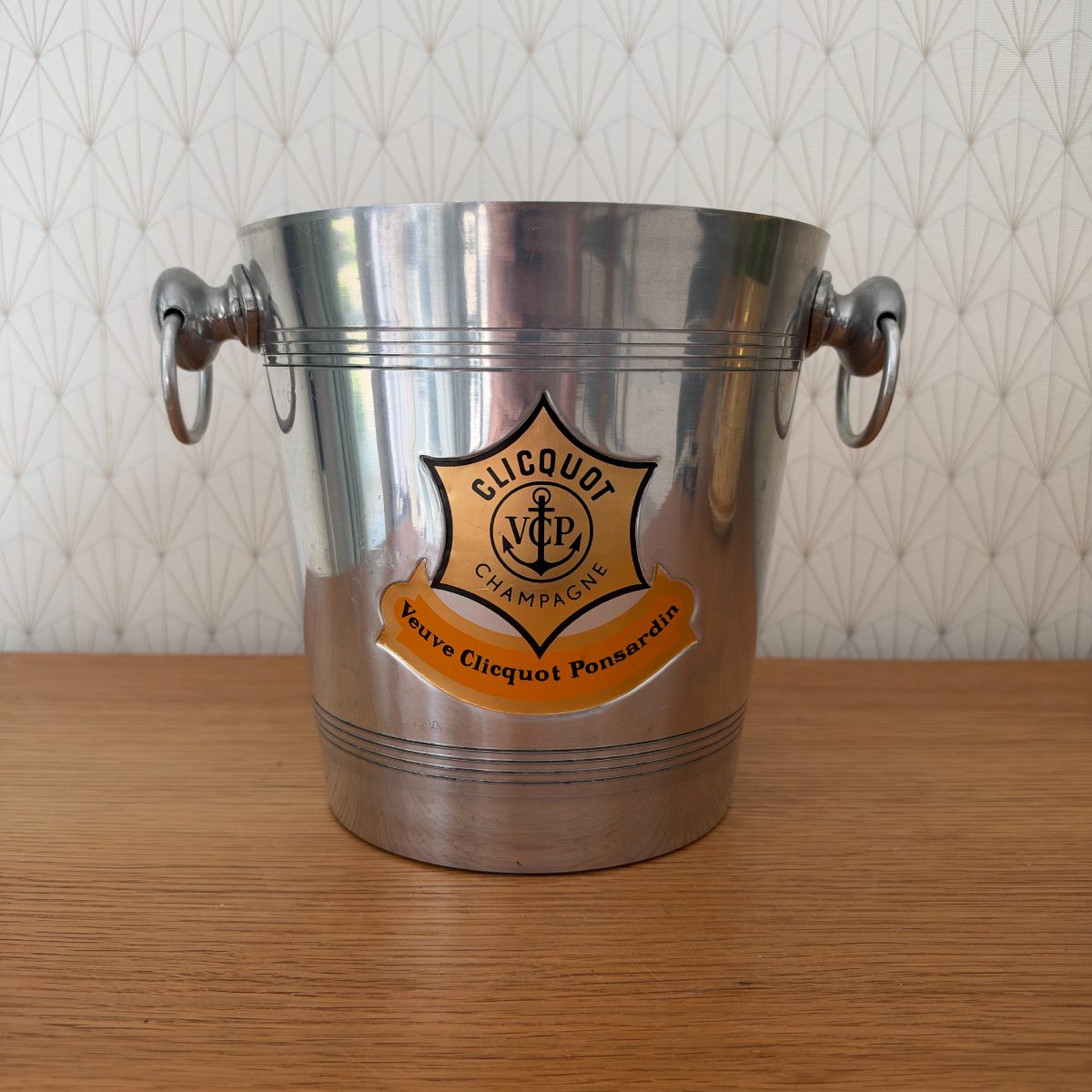 Second front view of Veuve Clicquot aluminium champagne ice bucket showing orange and black shield logo and ring handles clearly.